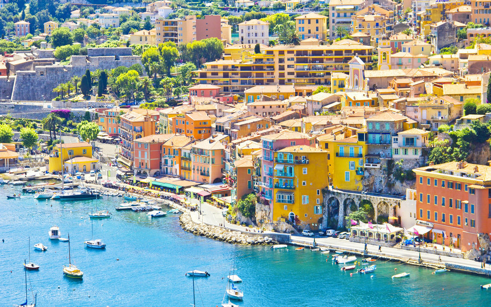 Houses coloured in shades of yellow and orange line the bay in the Mediterranean village of Eze as it rises up away from the bay.