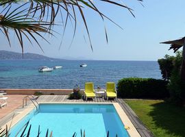 Looking across the pool to the wooden terrace and two yellow sunloungers with the Mediterranean sea and three large motorboats in the background.