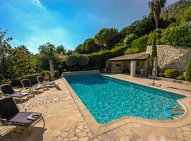 A large pool set into a private stone terrace with 4 beach loungers on the left nestles into the surrounding lush green landscape.
