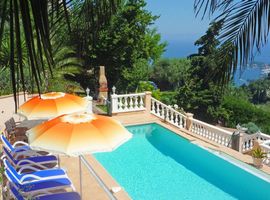5 blue sunloungers with umbrellas around the pool on a terrace that looks out from this Mediterranean holiday villa with Villefranche Bay in the distance.